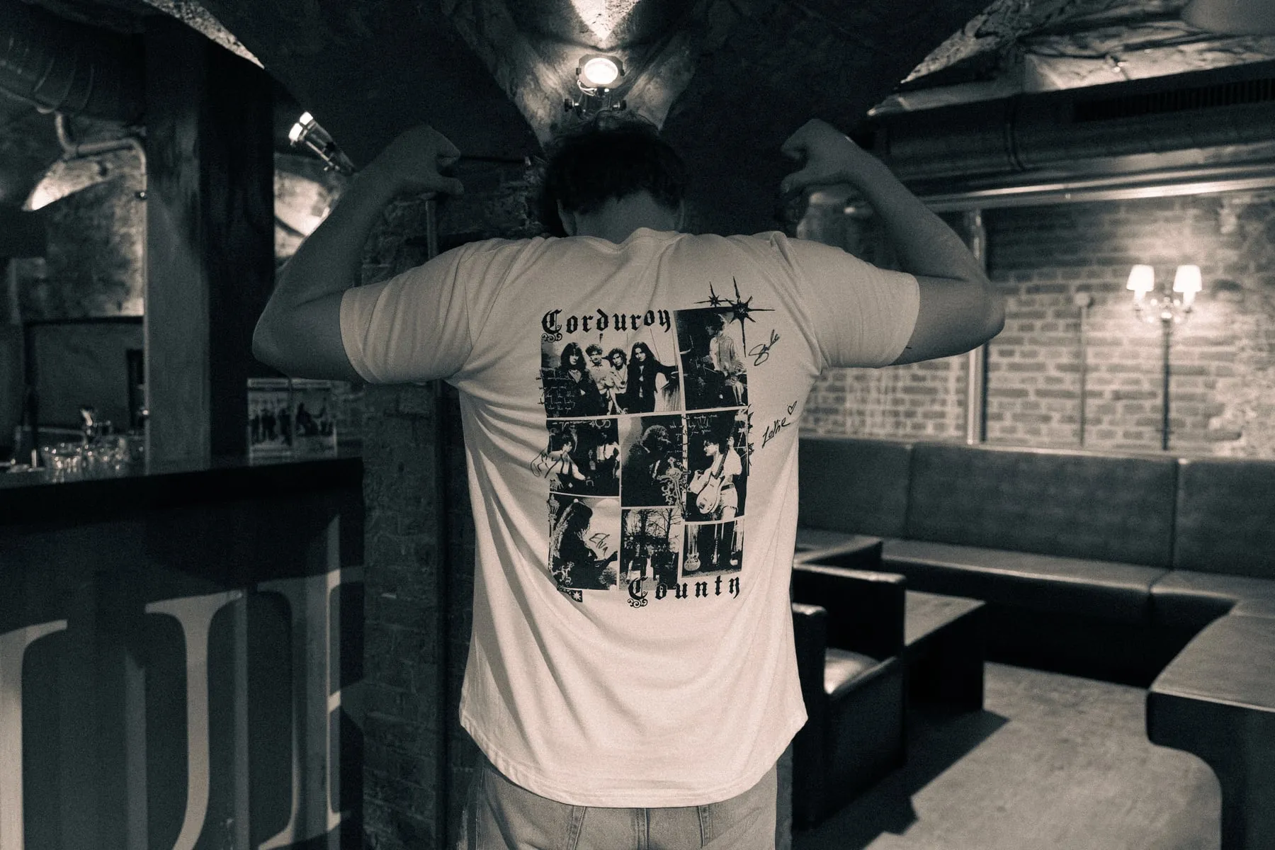 Someone in a bar, back to camera, showing the collage print across the back of the EP shirt.