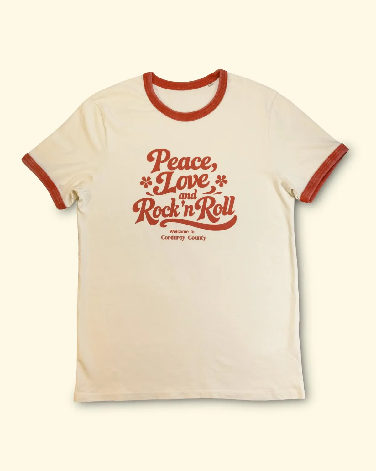 Natural ringer T-shirt with red trim, printed “Peace, Love and Rock ’n Roll — Welcome to Corduroy County”.